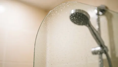 Arrière-plan lumineux montrant une paroi de douche en verre transparent, des gouttelettes d'eau sur la surface et une robinetterie métallique brillante.
