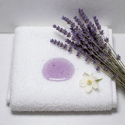 Serviette blanche pliée avec une goutte d'huile aromatique de lavande et jasmin, branches de lavande sèche et une fleur de jasmin blanc sur fond blanc et gris clair, idéal pour massages et spa.