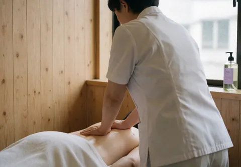 Thérapeute pratiquant un massage suédois dans une salle de spa aux murs en bois, avec un client en vêtements blancs et une lumière naturelle.