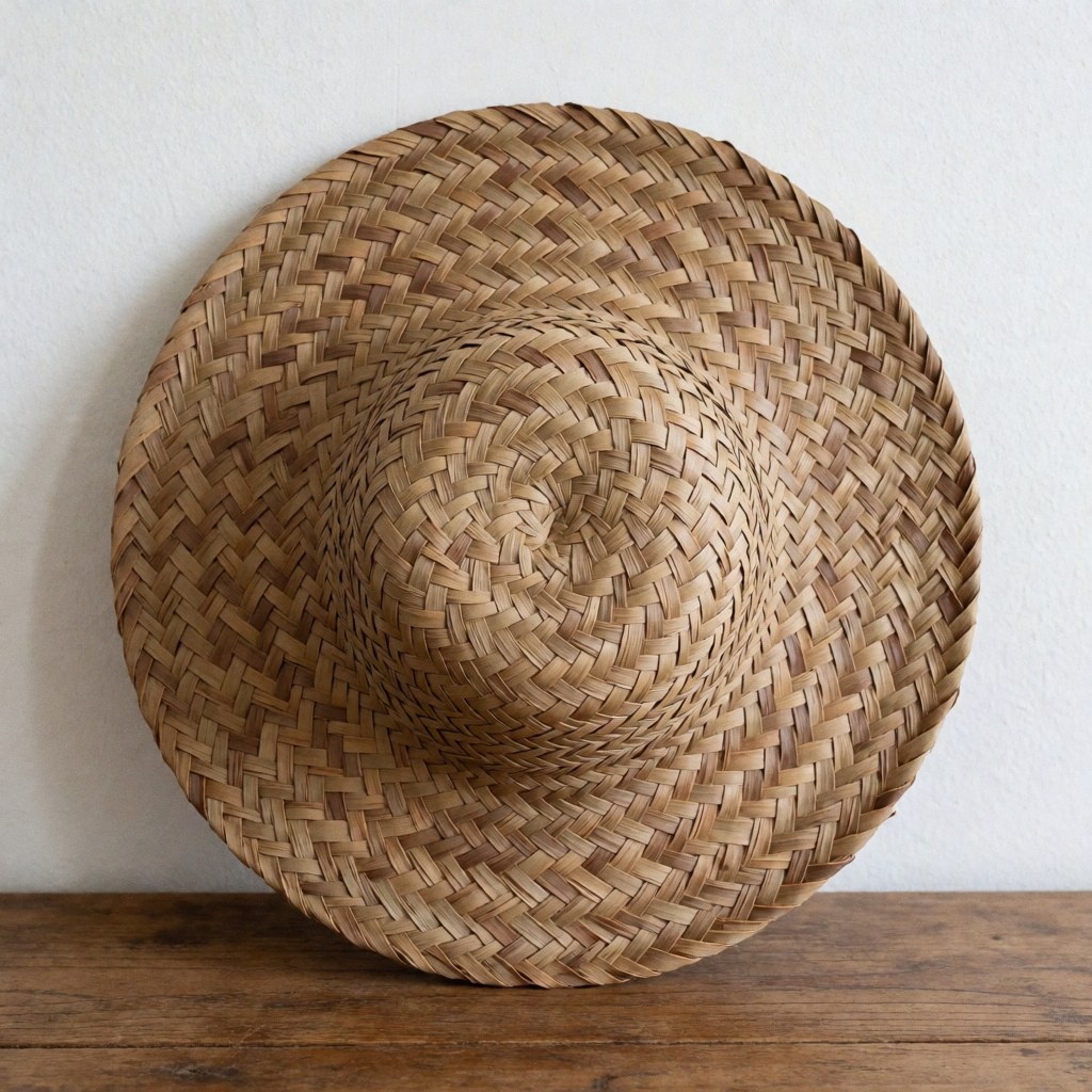 Un chapeau de paille tressé à la main est posé sur une surface en bois, mettant en valeur le travail artisanal et la texture naturelle du matériau.