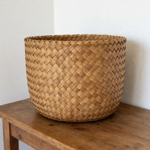 Un panier rond en paille naturelle posé sur une surface claire, offrant une vue détaillée de la texture tissée et des tons bruns.