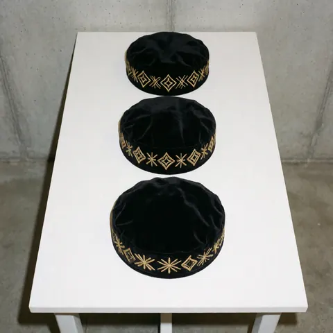 Trois casquettes noires en velours avec des broderies dorées disposées en ligne sur une surface blanche, idéales pour la personnalisation de vêtements.