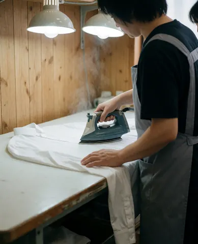 Un travailleur effectue un repassage professionnel d'une chemise blanche à l'aide d'un fer à repasser sur une table en bois.