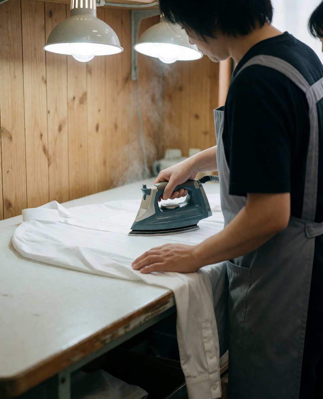 Un travailleur effectue un repassage professionnel d'une chemise blanche à l'aide d'un fer à repasser sur une table en bois.