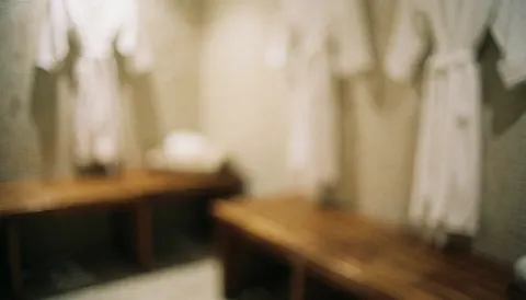 Intérieur d'un vestiaire de spa avec des bancs en bois et des serviettes blanches suspendues, éclairage chaleureux et ambiance relaxante.