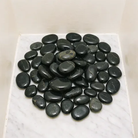 Plusieurs pierres noires en basalte disposées sur une surface blanche lisse, évoquant un environnement de spa professionnel.