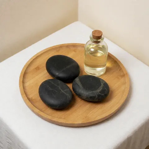 Ensemble de soins avec pierres volcaniques noires, huile essentielle en flacon verre et bouchon liège posés sur plateau bois rond.