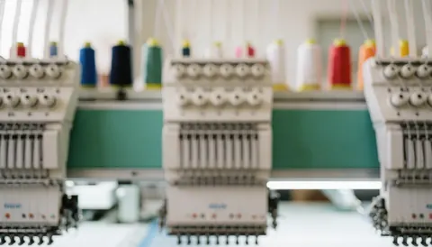 Vue rapprochée de bobines de fil colorées disposées sur une surface professionnelle, servant de fond texturé pour l'intégration de textes ou de graphiques dans le secteur de la personnalisation vestimentaire.