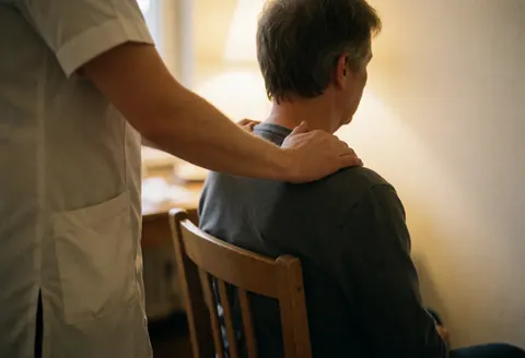 Un thérapeute professionnel masse le dos d'un client assis sur une chaise en bois dans un intérieur aux tons chauds et à l'atmosphère relaxante.