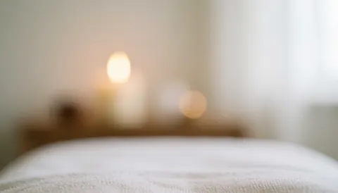 Arrière-plan de massage thaïlandais avec lit blanc et bougie allumée, lumières douces et bokeh, idéal pour textes sur relaxation et bien-être.