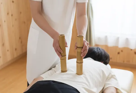 Thérapeute professionnel utilisant des tubes de bambou pour un massage relaxant sur le dos d'un client dans un spa calme.
