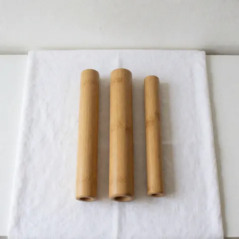 Trois tubes de massage thaïlandais en bambou, propres et prêts à l'emploi, posés sur un tissu blanc pour spa et bien-être.