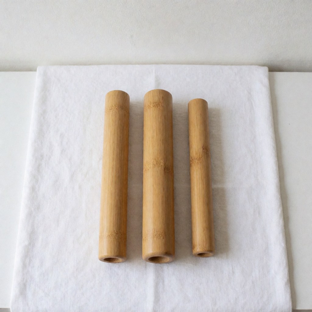 Trois tubes de massage thaïlandais en bambou, propres et prêts à l'emploi, posés sur un tissu blanc pour spa et bien-être.