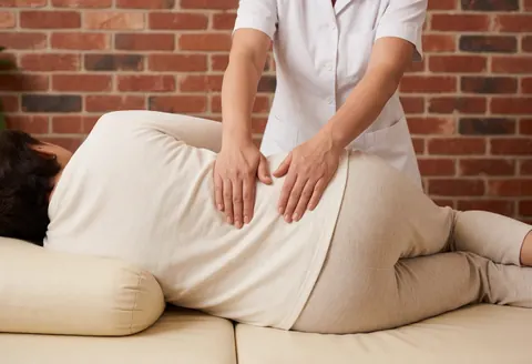 Une thérapeute réalise un massage thaïlandais doux sur une femme enceinte allongée sur un lit de massage dans un studio aux murs de briques.