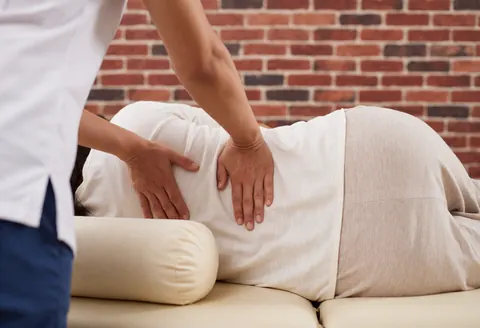Un thérapeute professionnel réalise un massage du dos sur une cliente allongée, utilisant ses mains pour travailler les muscles de la colonne vertébrale.