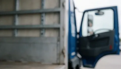 Arrière-plan industriel flou montrant une zone de chargement avec un camion et une grue, évoquant le secteur de la logistique et du transport professionnel.