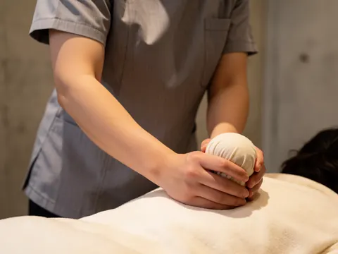Un thérapeute professionnel applique une boule d'herbes chaudes sur le dos nu d'un client lors d'une séance de massage relaxant.