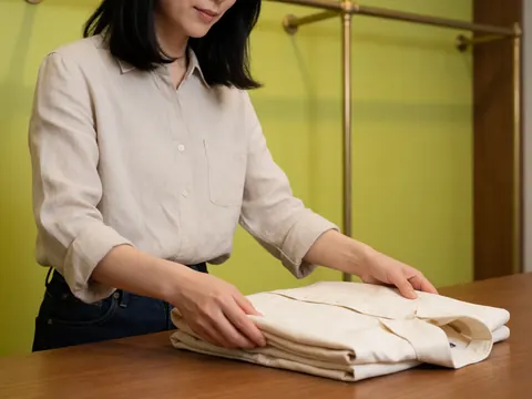 Des mains plient soigneusement un vêtement en tissu, mettant en valeur le travail artisanal et les détails du textile dans un contexte de boutique.