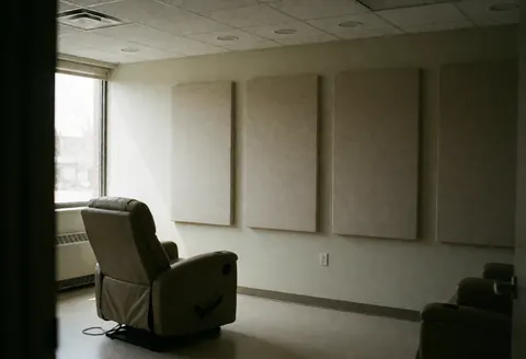 Intérieur d'une salle de thérapie calme équipée d'un fauteuil inclinable, de panneaux acoustiques aux murs et d'une fenêtre laissant entrer la lumière naturelle.