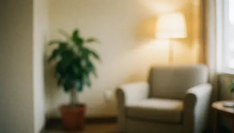 Un fauteuil beige est placé à côté d'une plante verte devant un mur de couleur chaude, créant une ambiance calme et accueillante.