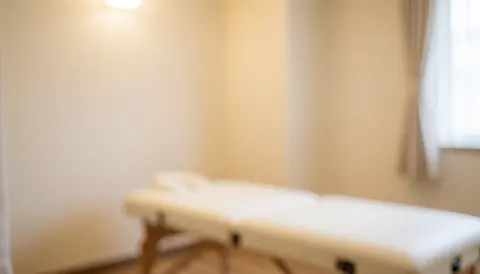 Vue d'un intérieur apaisant avec un lit de massage blanc sur fond beige, idéal pour illustrer les services de soins et de bien-être.