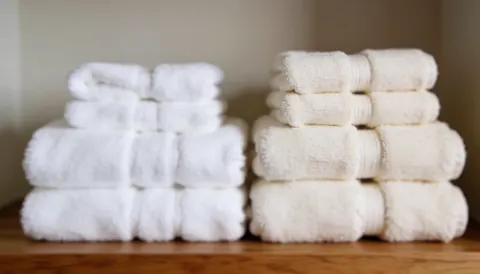Deux piles de serviettes blanches et naturelles posées sur une étagère en bois avec un fond doux et flou, idéal pour les textes de massage ayurvédique et de bien-être.