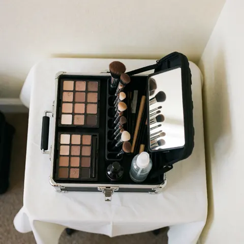 Kit de maquillage professionnel ouvert sur une table blanche, avec palette, pinceaux, miroir et spray, prêt pour les événements.