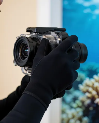 Gloves noirs tenant fermement un appareil photo sous-marin professionnel prêt à être utilisé pour des prises de vues en milieu aquatique.
