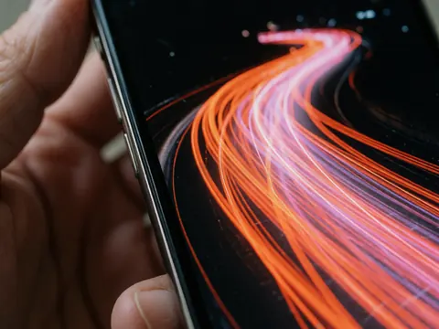 Gros plan d'un smartphone avec écran lumineux en longue exposition, mains visibles, haute résolution, effet de lumière orange et rose sur fond noir.