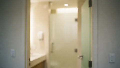 Arrière-plan de salle de bain avec lumière chaude, murs neutres et porte en verre, idéal pour des textes sur l'hypnothérapie ou les services professionnels.