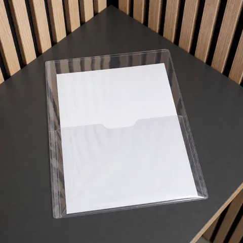 Couverture plastique transparente avec fenêtre avant posée sur une table noire, idéale pour présenter des thèses ou rapports, sur fond de lattes de bois clair.