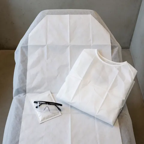 Lit de traitement avec serviette jetable, vêtements de protection et lunettes de sécurité. Scène propre et professionnelle pour épilation laser en clinique.