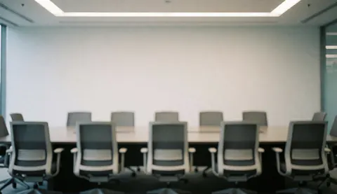 Salle de réunion moderne avec chaises vides et longue table, fond flou idéal pour textes corporatifs, lumières au plafond et murs blancs.