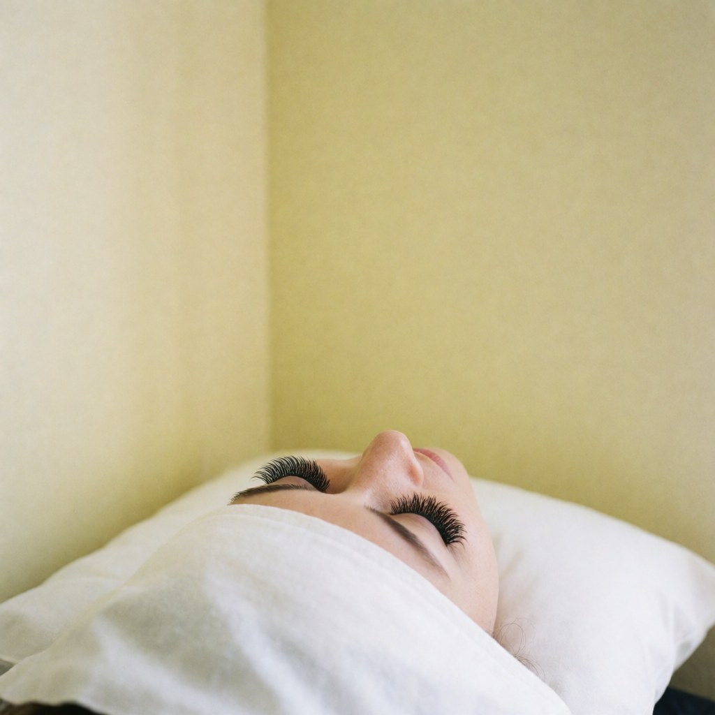 Yeux aux longs cils postiches volumineux reposant sur un oreiller blanc, fond jaune clair et éclairage doux pour un résultat beauté quotidien.