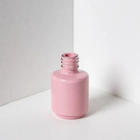 Flacon d'émail à ongles rose ouvert posé sur une surface blanche avec un fond uni, éclairage doux et professionnel pour catalogue de produits.