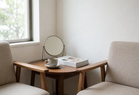 Miroir rond posé sur une table en bois clair entre deux chaises, accompagné d'une tasse de café et de magazines, baigné de lumière naturelle.