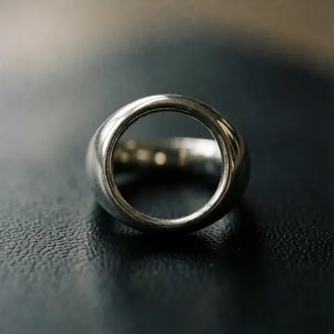 Une bague en métal poli aux reflets lumineux repose sur une surface en cuir noir texturé, éclairée de manière dramatique avec un flou d'arrière-plan.