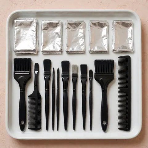 Vue de dessus d'outils professionnels de coiffure : brosses, peignes et feuilles sur un plateau blanc posé sur un mur en terre cuite.