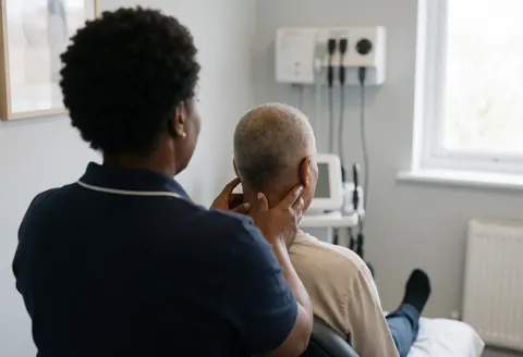 Un thérapeute applique un massage des tissus profonds sur le cou d'un client assis dans une clinique avec du matériel médical en arrière-plan.