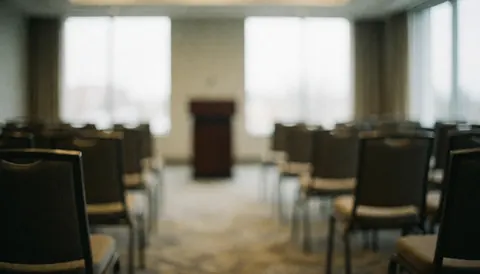 Salle de conférence professionnelle avec rangées de chaises et podium en arrière-plan, éclairage naturel par les fenêtres, idéal pour textes corporatifs