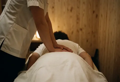 Un thérapeute professionnel effectue un massage sur le dos d'un client recouvert d'une serviette blanche dans un espace aux murs en bois.