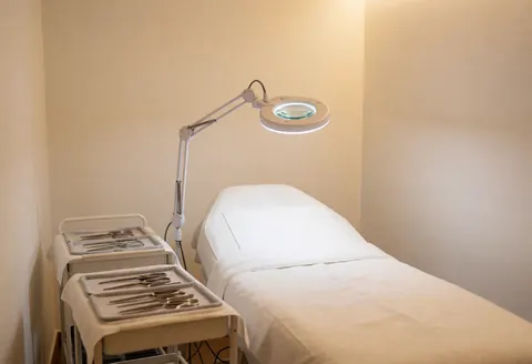 Salle de soin pour l'acné équipée de lits stériles, d'un éclairage grossissant et de plateaux à instruments dans un environnement propre et professionnel.