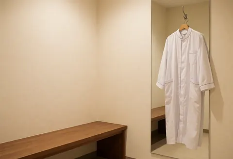 Intérieur d'une clinique avec banc en bois, miroir et blouse blanche suspendue, éclairage chaleureux pour un espace privé et accueillant.
