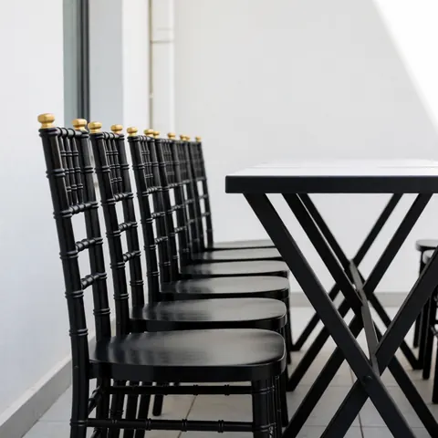 Chaises noires aux détails dorés alignées près d'une table moderne dans un patio extérieur minimaliste aux murs blancs.