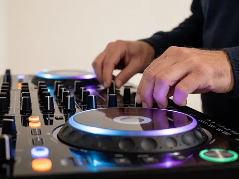 Gros plan sur un contrôleur dj éclairé par des lumières néon bleues et violettes, mains manipulant boutons et molettes dans un contexte professionnel.