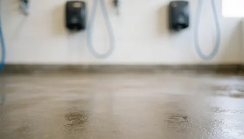Fond de lavage automobile avec sol en béton humide et distributeurs de savon flous sur le mur, éclairage doux et neutre idéal pour ajouter du texte.