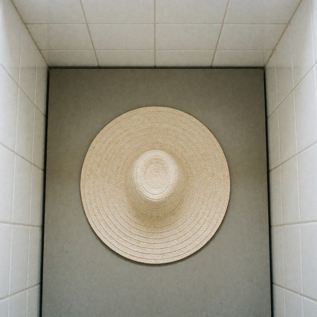 Chapeau vueltiao en paille au design circulaire posé sur une surface grise avec des murs de carreaux blancs, vue de dessus et éclairage diffus.