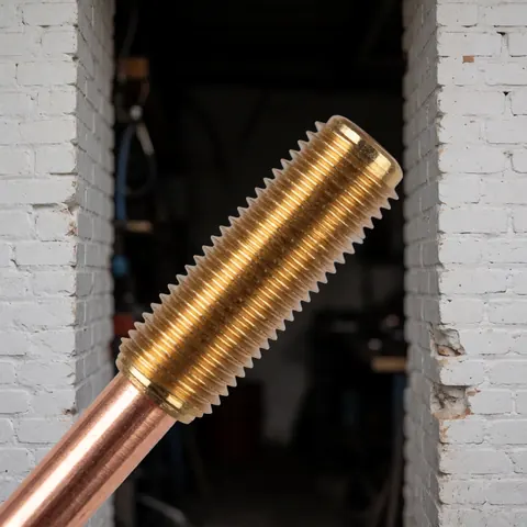 Gros plan d'un capteur thermocouple en bronze avec fils métalliques, posé sur un mur de briques blanches dans un atelier de réparation de cuisinières.