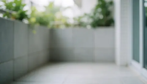 Arrière-plan de balcon extérieur avec murs de carreaux gris, sol carrelé et plantes vertes floues, éclairé par une lumière diffuse, idéal pour du texte commercial.
