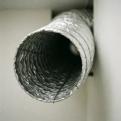 Conduit flexible HVAC avec armature en fil visible, isolé et fixé sur un mur blanc pour la réparation du chauffage.